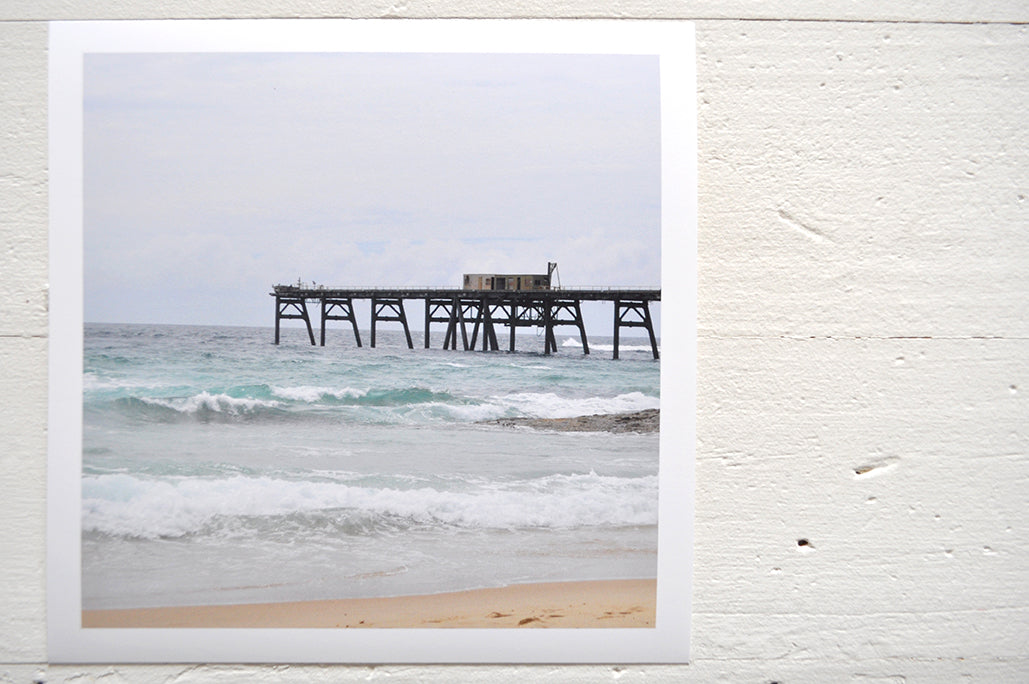 Pinch River unframed 17cm x 17cm Photographic Print on Paper Titled: Catherine Hill Bay Jetty. The subject of the print is the iconic Catherine Hill Bay Jetty from the beach, waves rolling in and beautiful aqua blue of the water in the background. Top view.