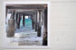 Pinch River unframed 17cm x 17cm Photographic Print on Paper Titled: Underneath the Jetty #2. The subject of the print is a close-up of the iconic Catherine Hill Bay Jetty from underneath, with the weather-worn timber pilings, waves rolling in and beautiful aqua blue of the water in the background. Top view.