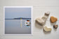 Photographic Print on Paper Titled: Nautical Reflections. The subject of the print is a boat docked at a marina and reflections on the still lake water. Top view with love heart shaped stones to style the product image.