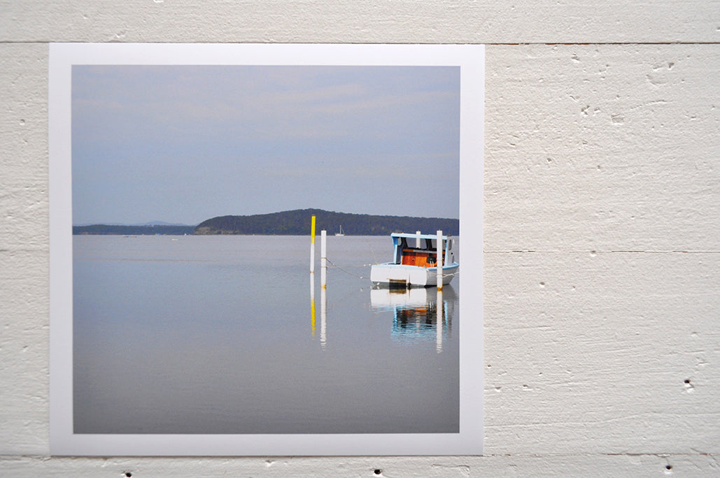 Photographic Print on Paper Titled: Nautical Reflections. The subject of the print is a boat docked at a marina and reflections on the still lake water. Top view.