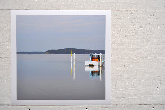 Photographic Print on Paper Titled: Nautical Reflections. The subject of the print is a boat docked at a marina and reflections on the still lake water. Top view.