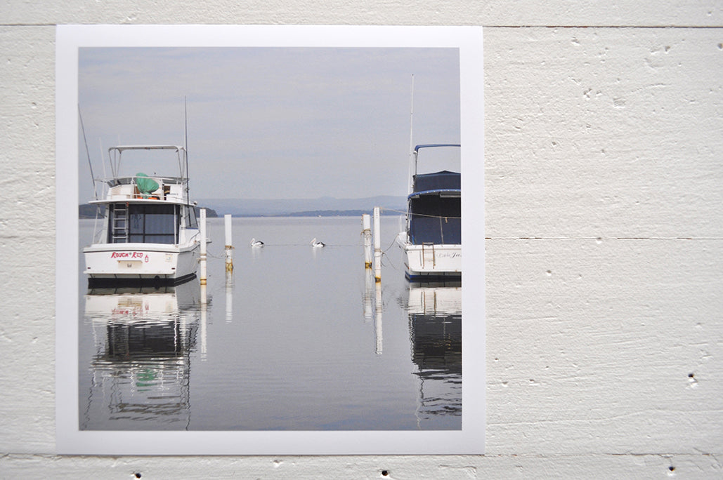 Pinch River unframed 17cm x 17cm Photographic Print on Paper Titled: Lakeside Cruising #2. The subject of the print is pelicans and boats docked at a marina with reflections on the still lake water. Top view.
