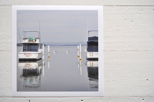 Pinch River unframed 17cm x 17cm Photographic Print on Paper Titled: Lakeside Cruising #2. The subject of the print is pelicans and boats docked at a marina with reflections on the still lake water. Top view.
