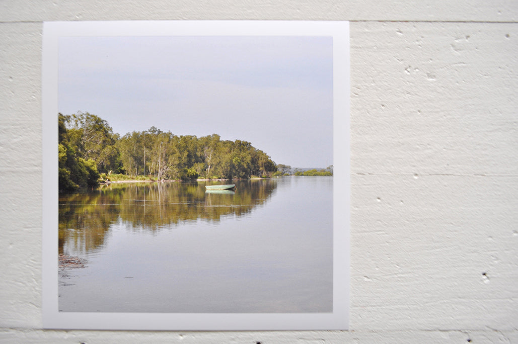 Pinch River unframed 17cm x 17cm Photographic Print on Paper Titled: The Green Boat. The subject of the print is a green row boar on the lake, with reflections of the treed shoreline on the still lake water. Top view.
