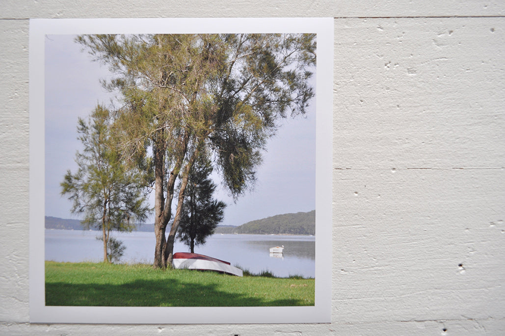 Pinch River unframed 17cm x 17cm Photographic Print on Paper Titled: Waiting for Sunday #1. The subject of the print is a large tree on the lake shore with an upturned row boat underneath it. Top view.
