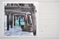 Pinch River unframed 17cm x 17cm Photographic Print on Paper Titled: Underneath the Jetty #1. The subject of the print is a close-up of the iconic Catherine Hill Bay Jetty from underneath, with the weather-worn timber pilings, waves rolling in and beautiful aqua blue of the water in the background. Top view.