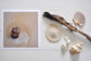 Pinch River unframed 17cm x 17cm Photographic Print on Paper Titled: Worn by the Tide. The subject of the print is a rusted metal post in the sand, in a pool of water. Top view with sea shells and driftwood next to it to style the product image.