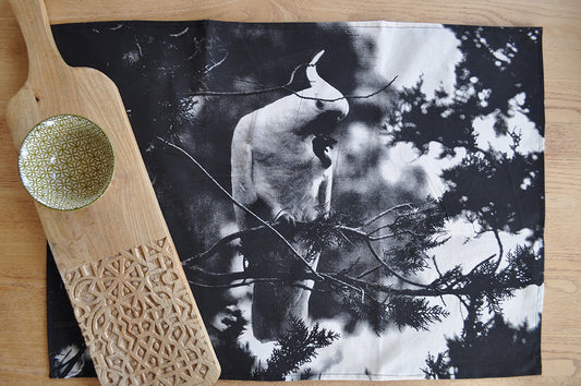 Pinch River handprinted halftone Cockatoo tea towel. Top view. Image styled with part engraved cutting board, and patterned bowl next to tea towel.