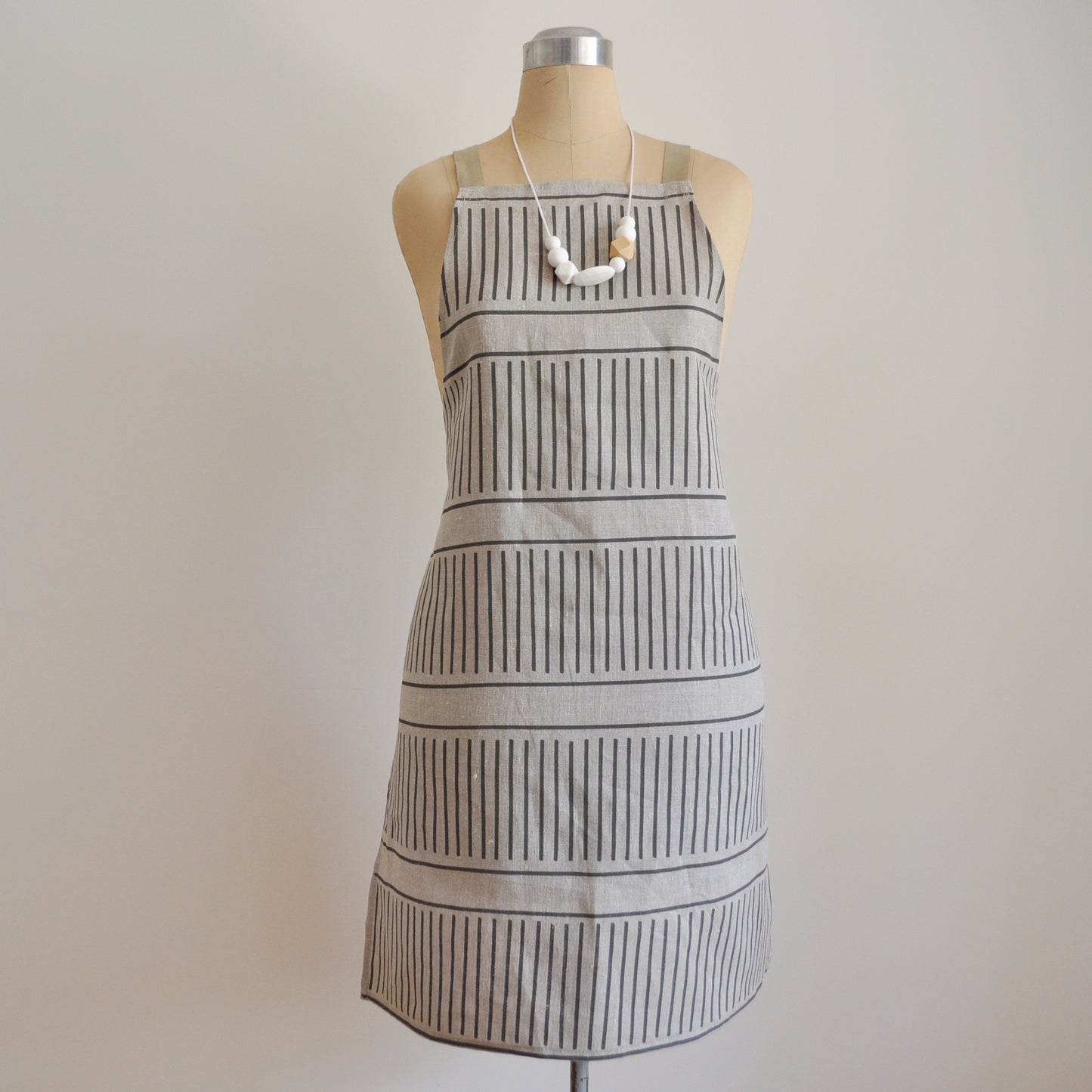 Pinch River bib apron / full apron in Corduroy Pathway print in Grey Bark on Natural Linen (colourway 2), on dressmakers dummy against a plain background. Front View.