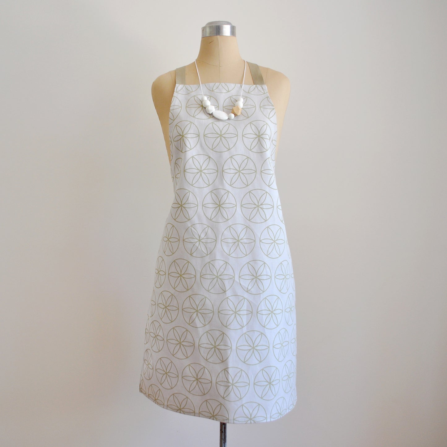 Pinch River bib apron / full apron in Flower of Life print, Spring Green on Silver Ash (colourway 1) on dressmakers dummy against a plain background. Front View.