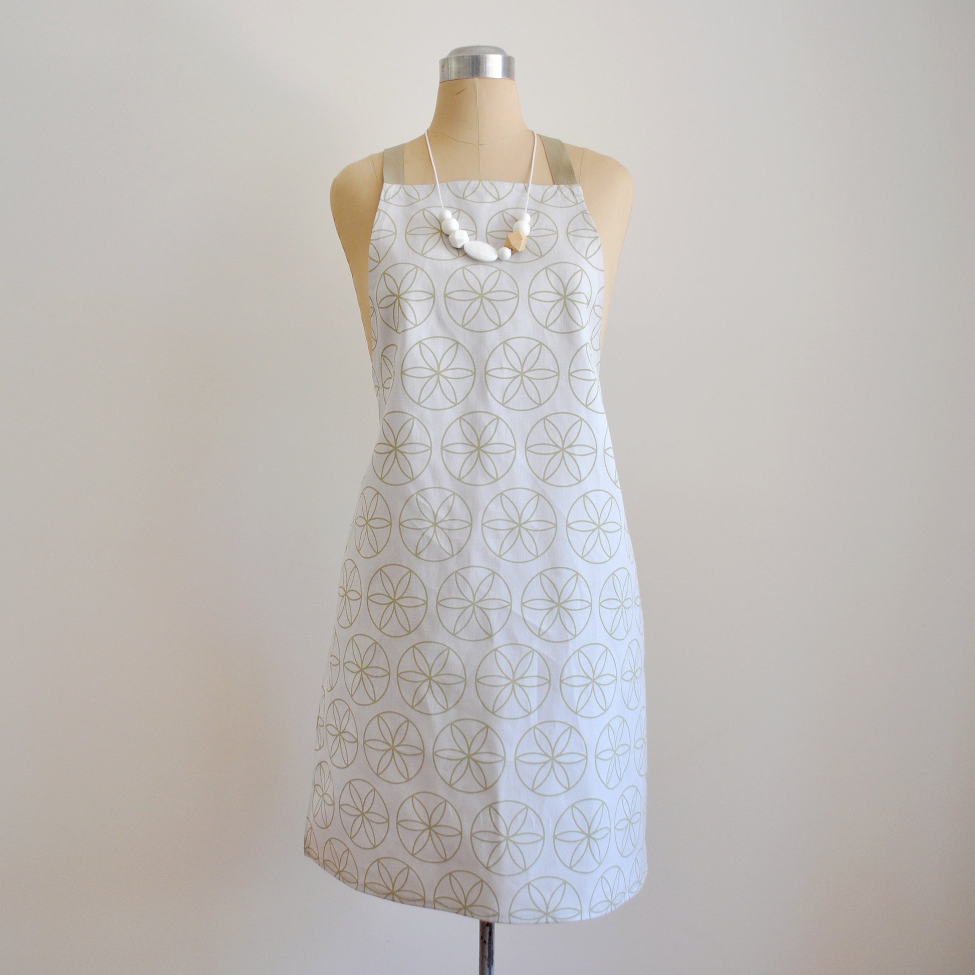 Pinch River bib apron / full apron in Flower of Life print, Spring Green on Silver Ash (colourway 1) on dressmakers dummy against a plain background. Front View.