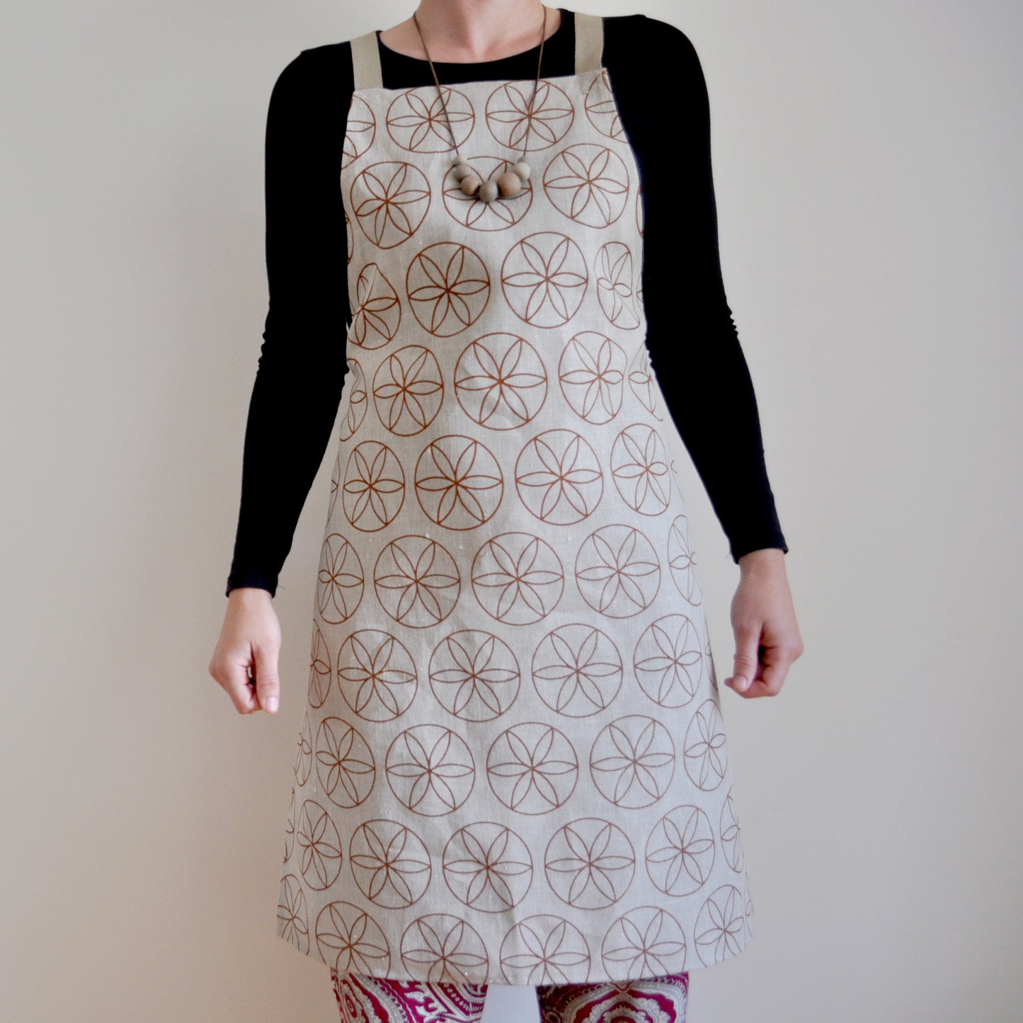 Model wearing Pinch River bib apron / full apron in Flower of Life print against a plain background. Front View. Pose #1