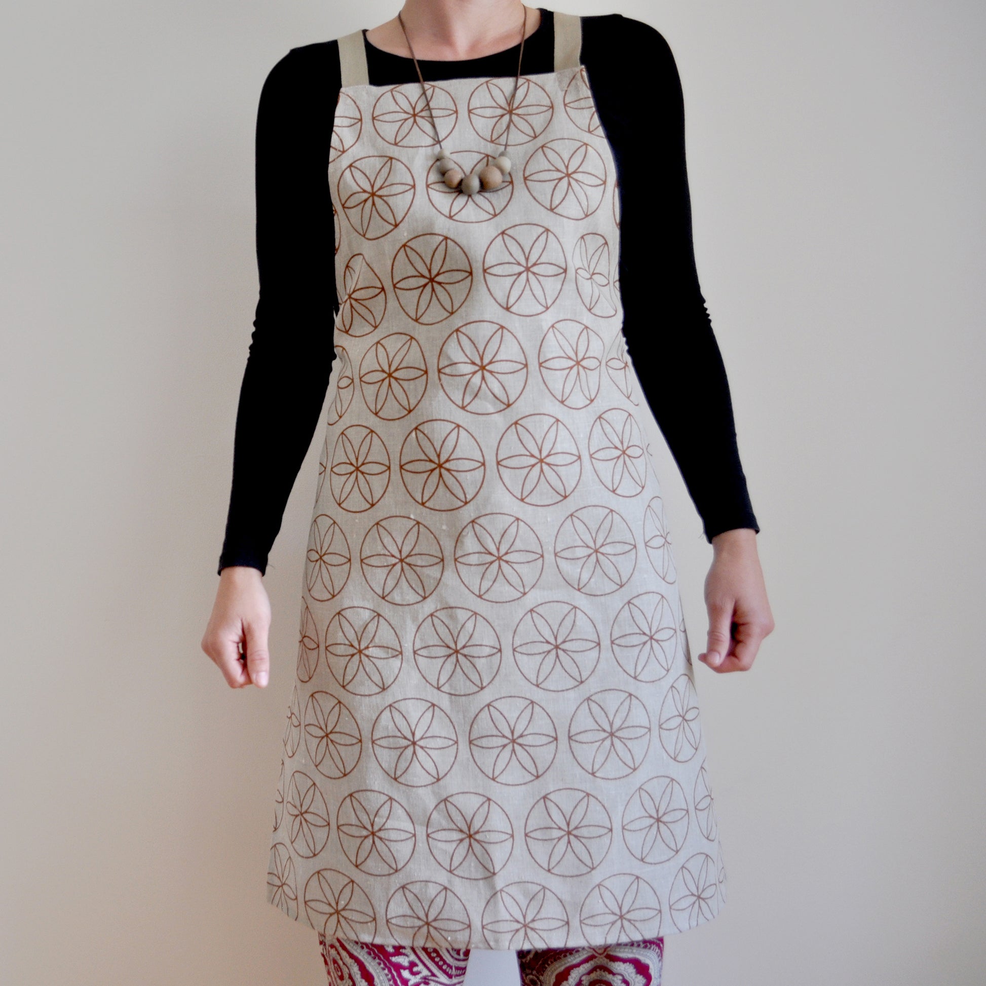 Model wearing Pinch River bib apron / full apron in Flower of Life print against a plain background. Front View. Pose #1
