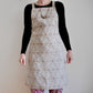 Model wearing Pinch River bib apron / full apron in Flower of Life print against a plain background. Front View. Pose #1