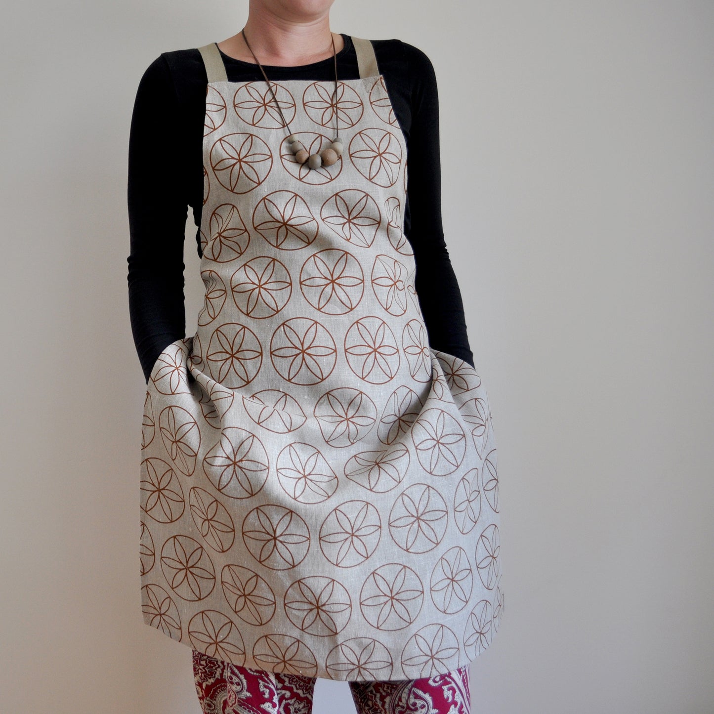 Model wearing Pinch River bib apron / full apron in Flower of Life print against a plain background. Front View. Pose #2