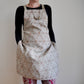 Model wearing Pinch River bib apron / full apron in Flower of Life print against a plain background. Front View. Pose #2