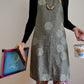 Model wearing Pinch River bib apron / full apron in Honeycomb print holding a a silk screen, squeegee and a tub of printing ink against a plain background. Front View.