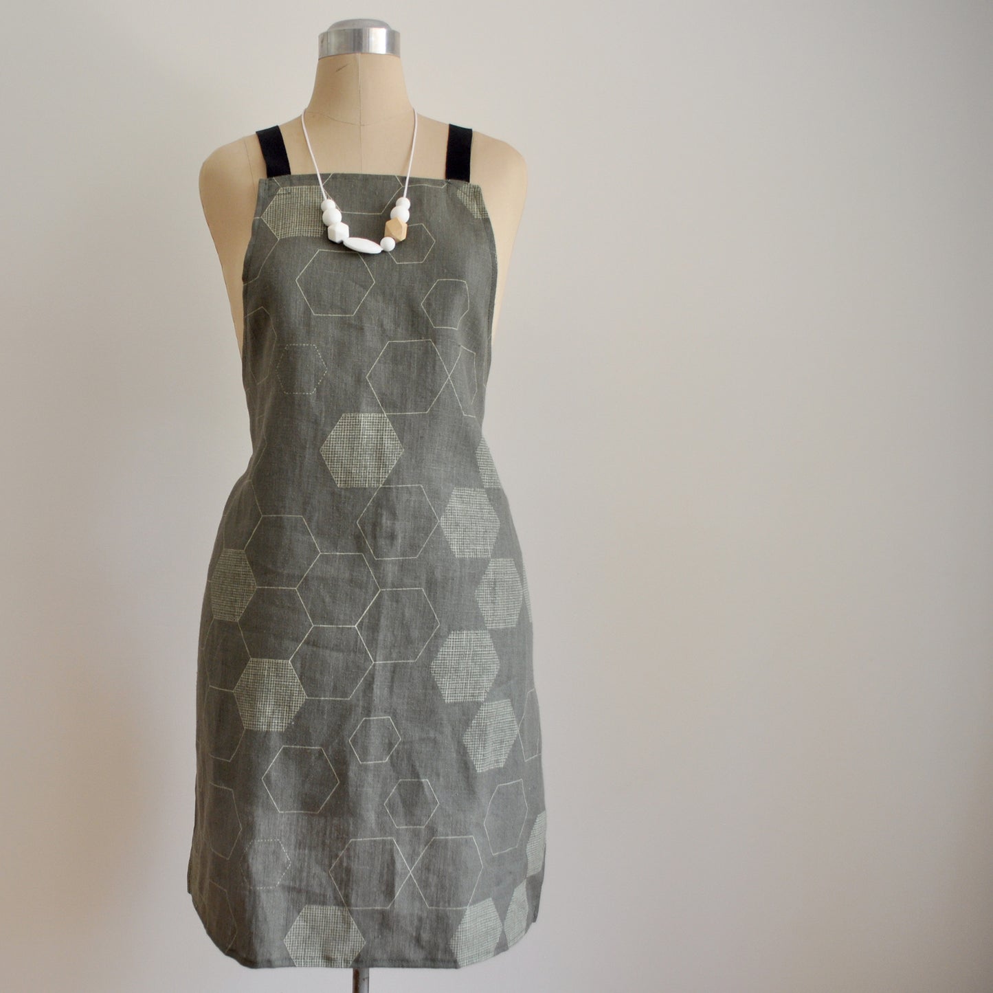 Pinch River bib apron / full apron in Honeycomb print, Chino on Forest Green Linen (colourway 2) on dressmakers dummy against a plain background. Front View.