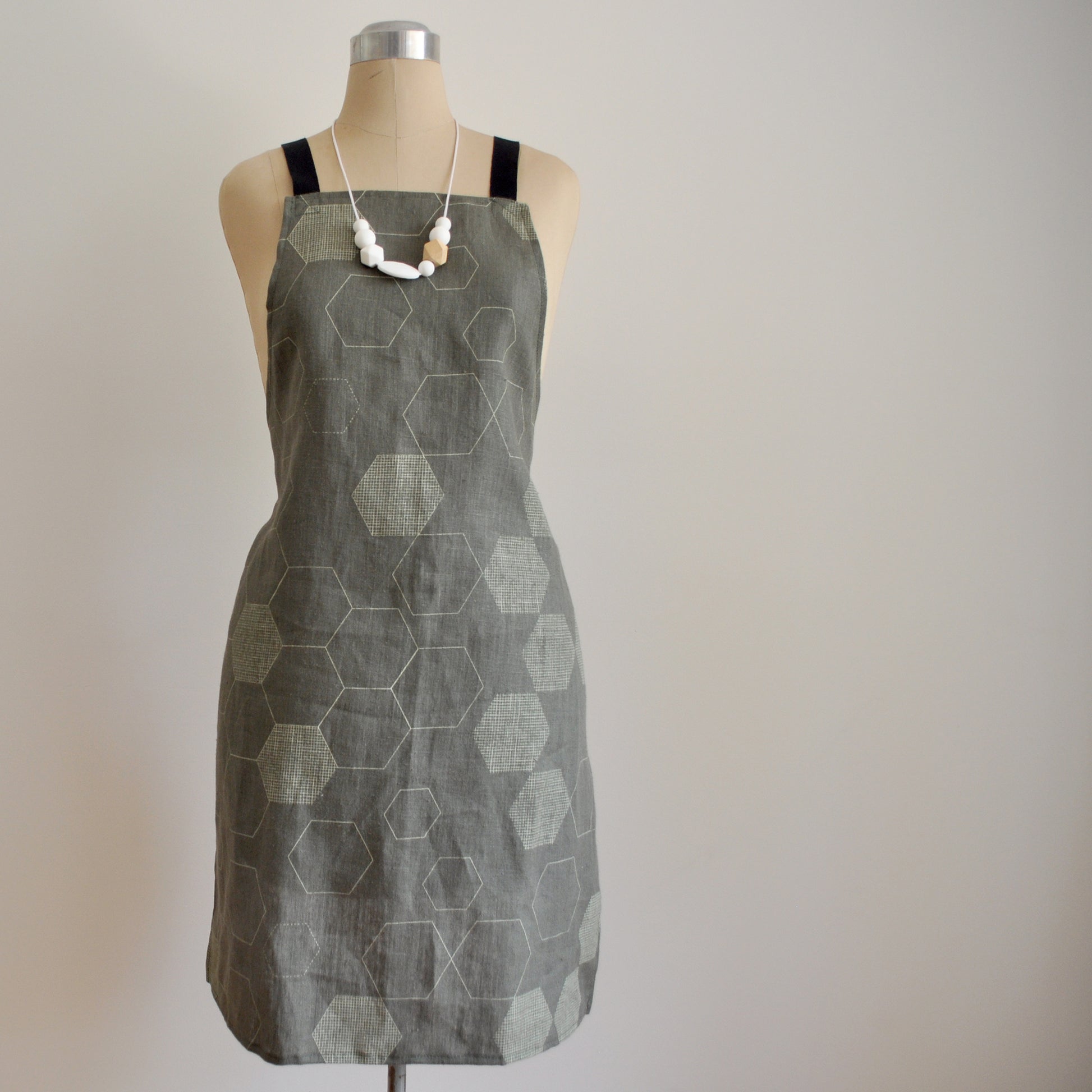 Pinch River bib apron / full apron in Honeycomb print, Chino on Forest Green Linen (colourway 2) on dressmakers dummy against a plain background. Front View.