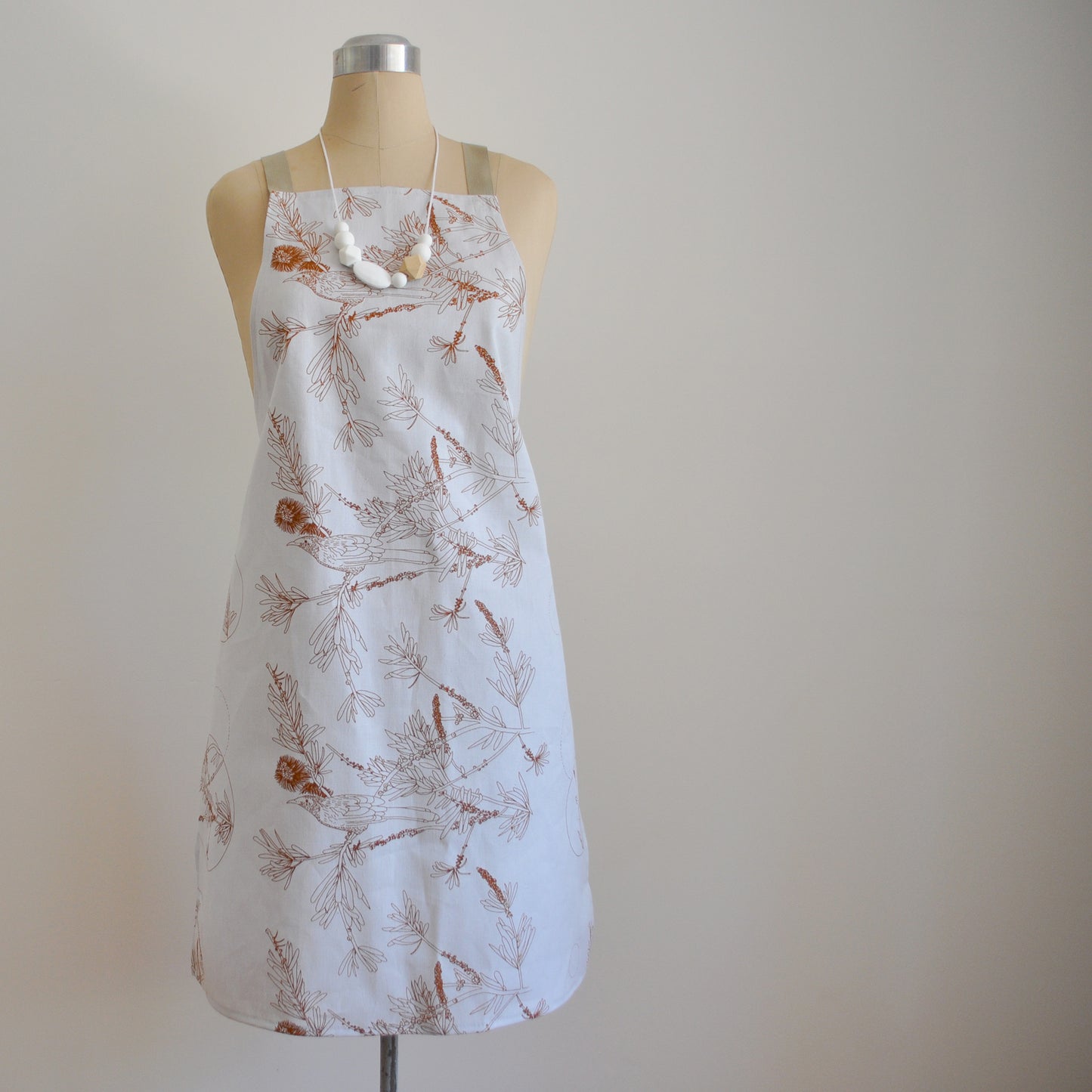 Pinch River bib apron / full apron in Wattle Bird in the Bottle Brush print, Burnt Orange on Silver Ash (colourway 2_v1) on dressmakers dummy against a plain background. Front View.