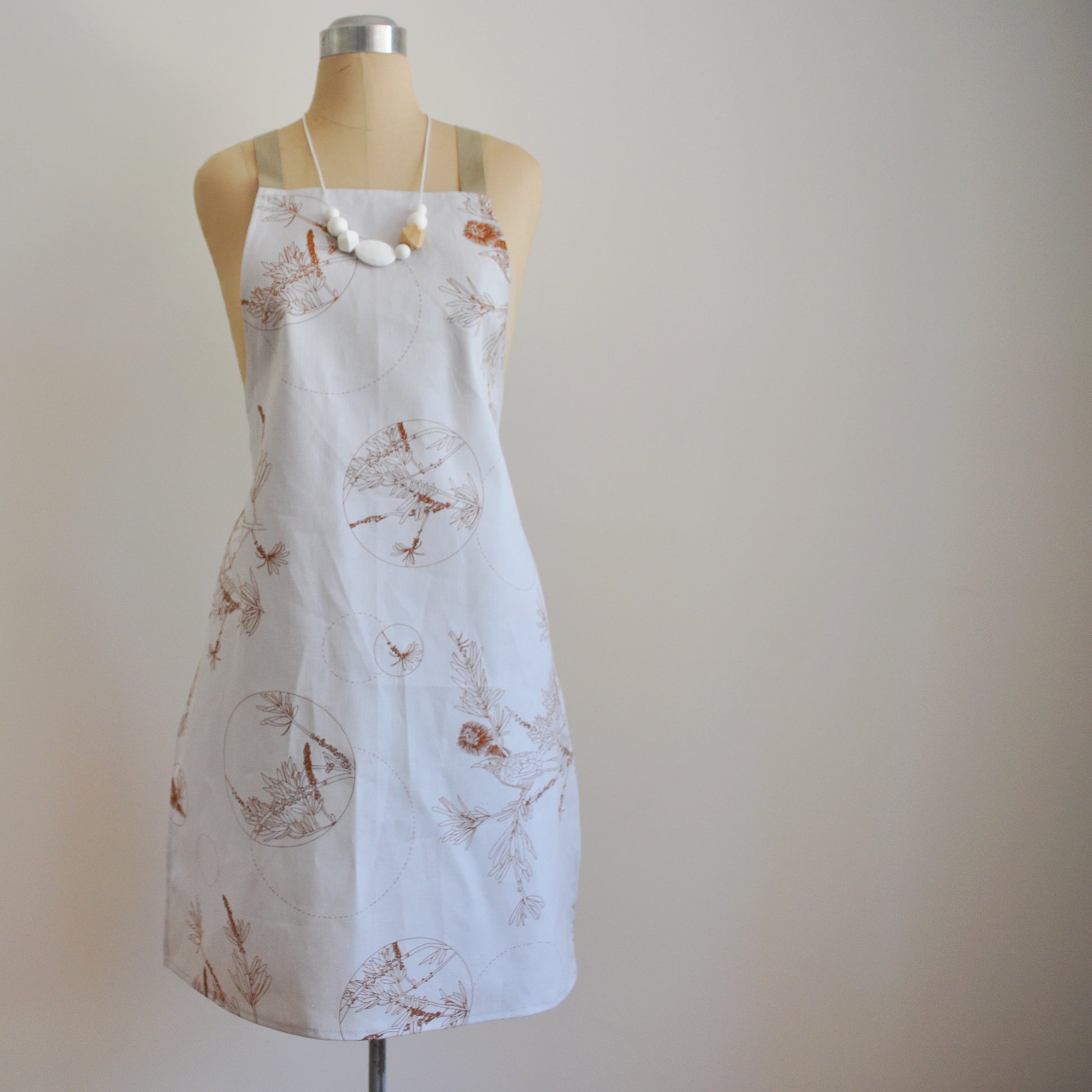 Pinch River bib apron / full apron in Wattle Bird in the Bottle Brush print, Burnt Orange on Silver Ash (colourway 2_v2) on dressmakers dummy against a plain background. Front View.