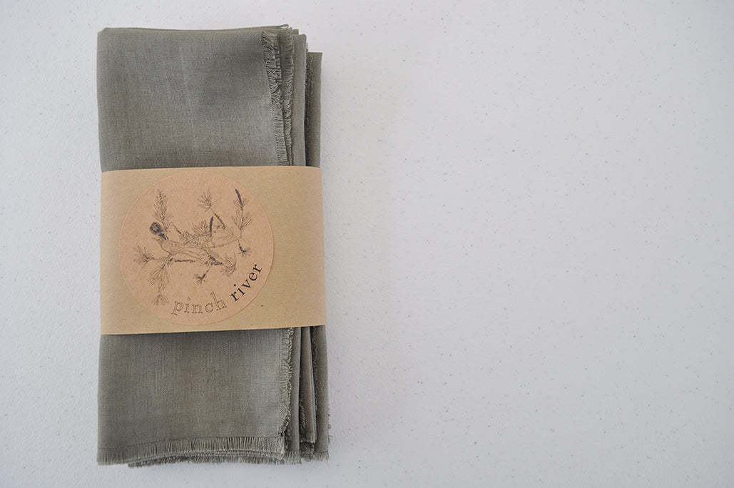 Set of 4 Pinch River pure linen napkins in Olive a branded belly band / product sleeve. Top view.