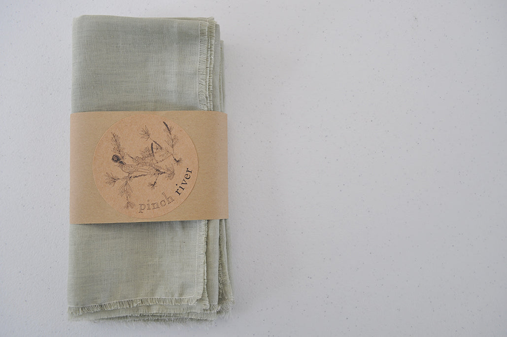 Set of 4 Pinch River pure linen napkins in Sage, in a branded belly band / product sleeve. Top view.