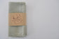 Set of 4 Pinch River pure linen napkins in Sage, in a branded belly band / product sleeve. Top view.