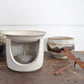 Ceramic essential oil burner. Product image is styled with ceramic pots in the background and a rusty dragonfly ornament in the foreground.