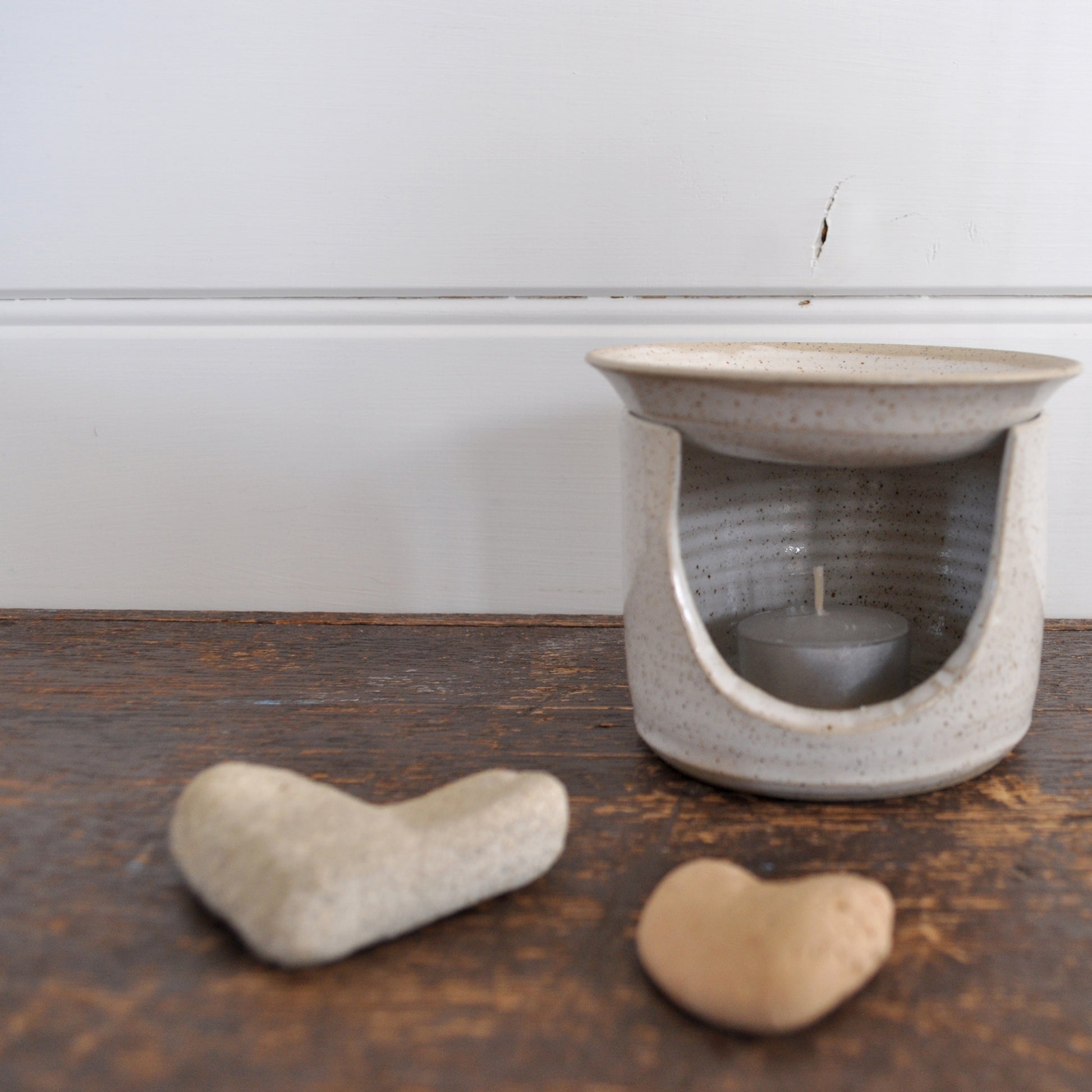 Ceramic essential oil burner. Product image is styled with love heart shaped stones in the foreground.