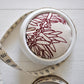 Pinch River ceramic pin cushion featuring Bottle Brush print in Wine Berry (colourway 1). Close-up top view. Product image is styled with a measuring tape.