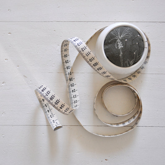 Pinch River ceramic pin cushion featuring Bottle Brush print in Moss Green (colourway 3). Top view. Product image is styled with a measuring tape and pins.