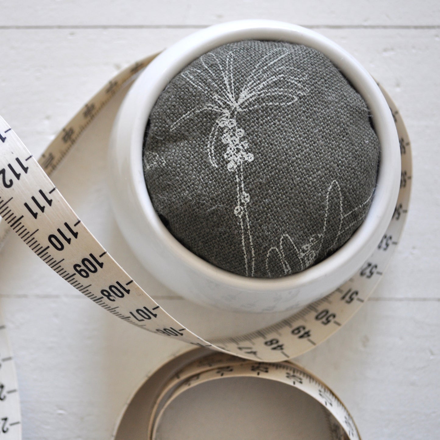 Pinch River ceramic pin cushion featuring Bottle Brush print in Moss Green (colourway 3). Close-up top view. Product image is styled with a measuring tape.