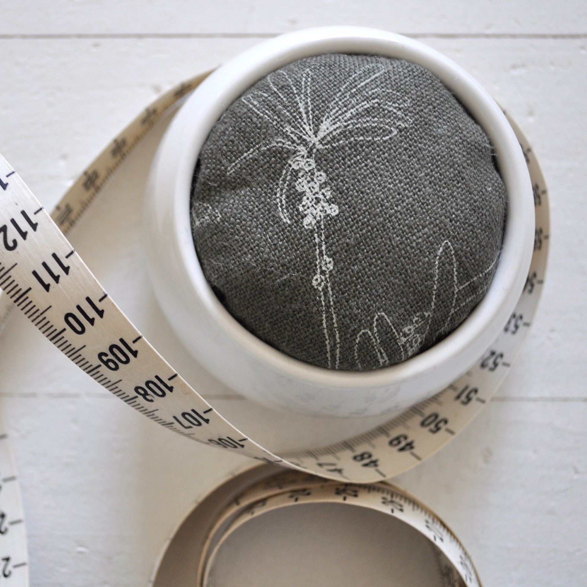 Pinch River ceramic pin cushion featuring Bottle Brush print in Moss Green (colourway 3). Close-up top view. Product image is styled with a measuring tape.