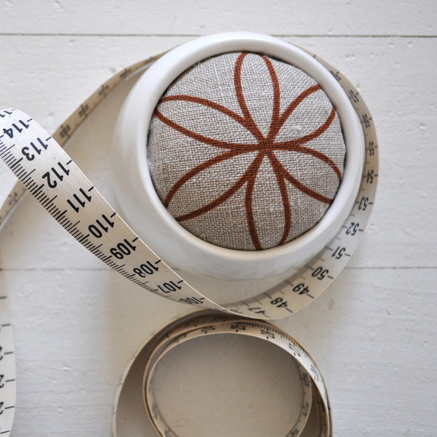 Pinch River ceramic pin cushion featuring Flower of Life print in Burnt Orange (colourway 2). Close-up top view. Product image is styled with a measuring tape.
