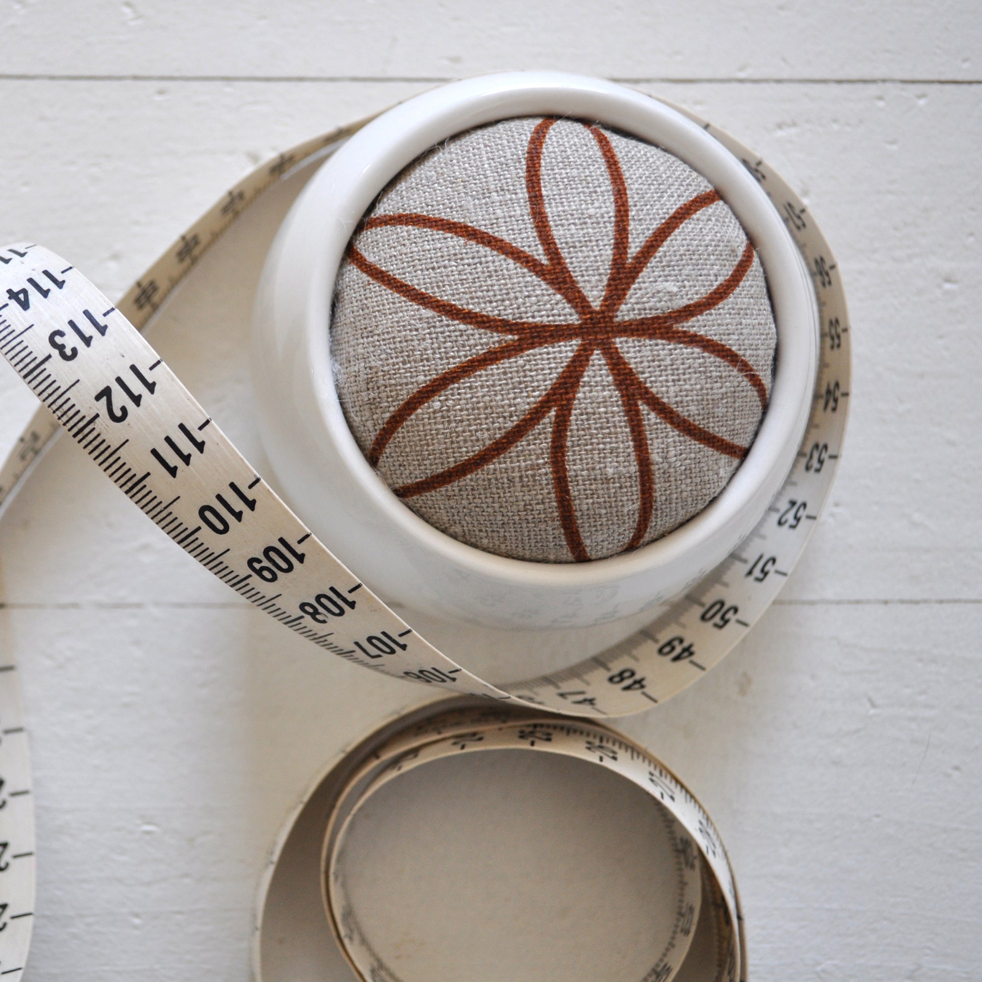 Pinch River ceramic pin cushion featuring Flower of Life print in Burnt Orange (colourway 2). Close-up top view. Product image is styled with a measuring tape.