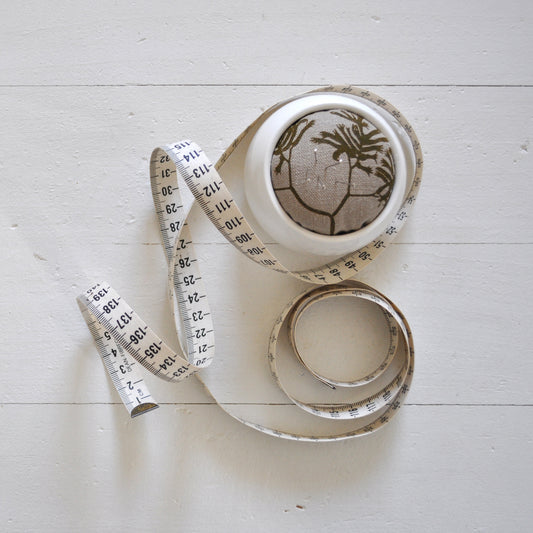 Pinch River ceramic pin cushion featuring Kangaroo Paw print in Desert Green (colourway 1). Top view. Product image is styled with a measuring tape and pins.