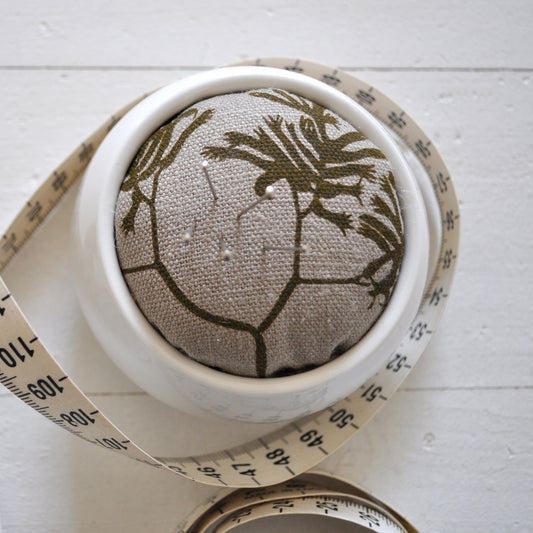 Pinch River ceramic pin cushion featuring Kangaroo Paw print in Desert Green (colourway 1). Close-up top view. Product image is styled with a measuring tape and pins.