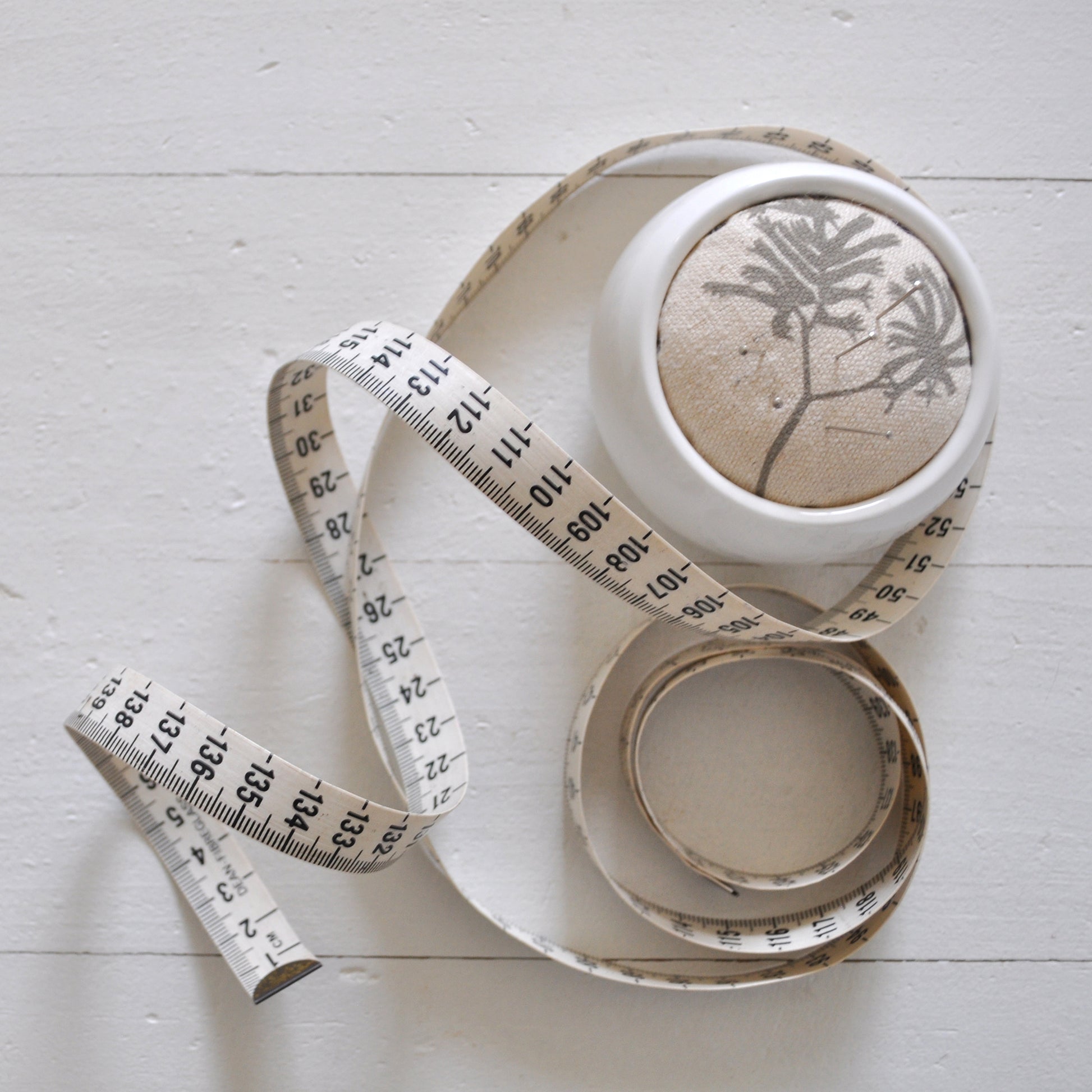 Pinch River ceramic pin cushion featuring Kangaroo Paw print in Aged Wood (colourway 2_v1). Top view. Product image is styled with a measuring tape and pins.