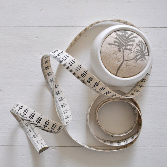 Pinch River ceramic pin cushion featuring Kangaroo Paw print in Aged Wood (colourway 2_v1). Top view. Product image is styled with a measuring tape and pins.