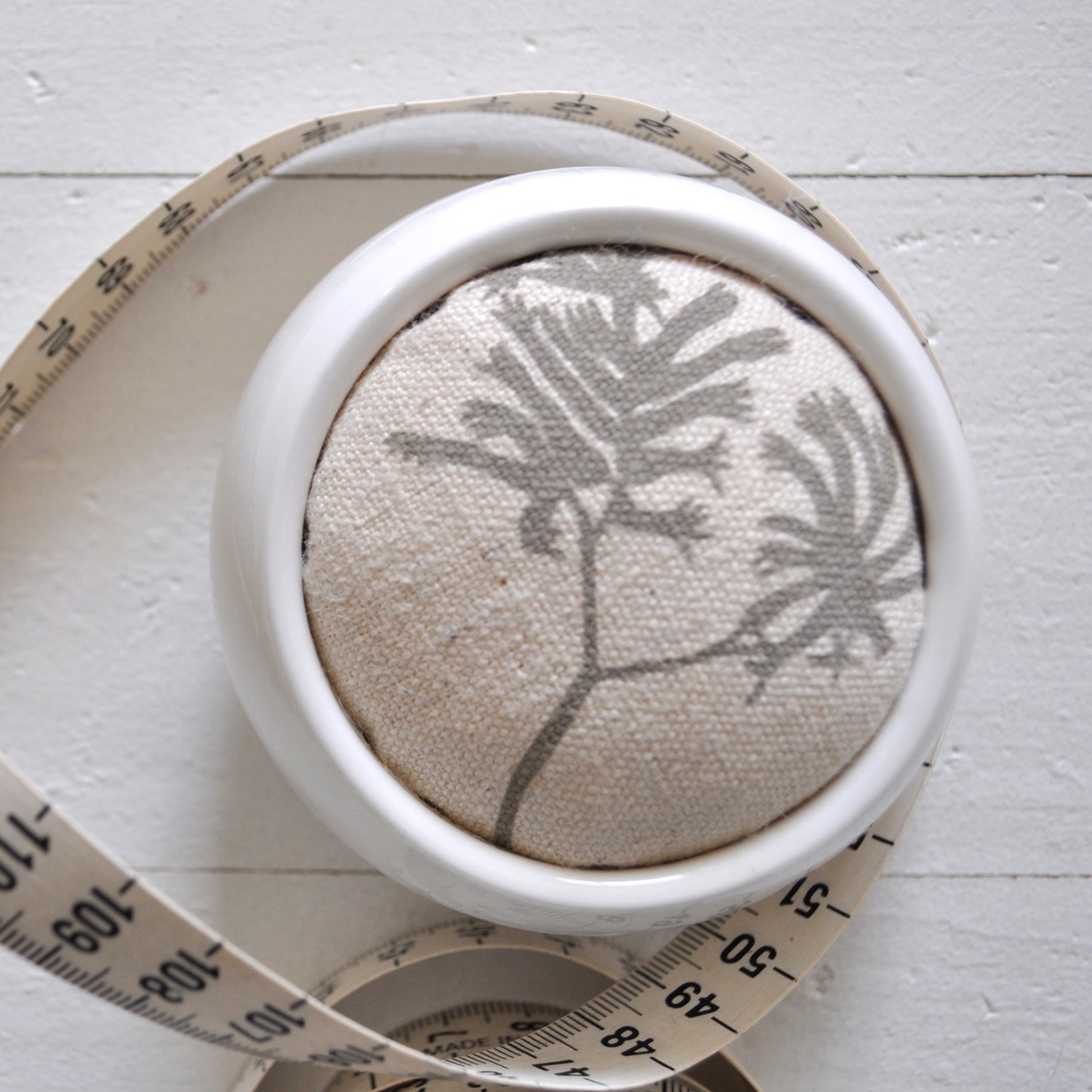 Pinch River ceramic pin cushion featuring Kangaroo Paw print in Aged Wood (colourway 2_v1). Close-up top view. Product image is styled with a measuring tape.
