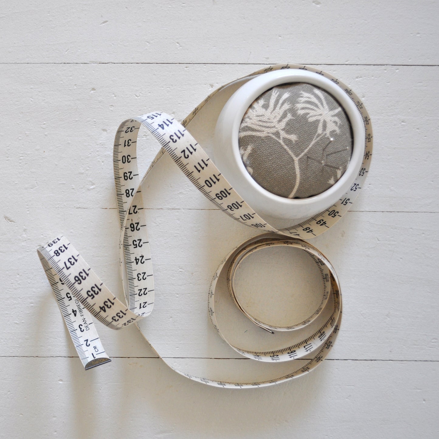 Pinch River ceramic pin cushion featuring Kangaroo Paw print in Aged Wood (colourway 2_v2). Top view. Product image is styled with a measuring tape and pins.