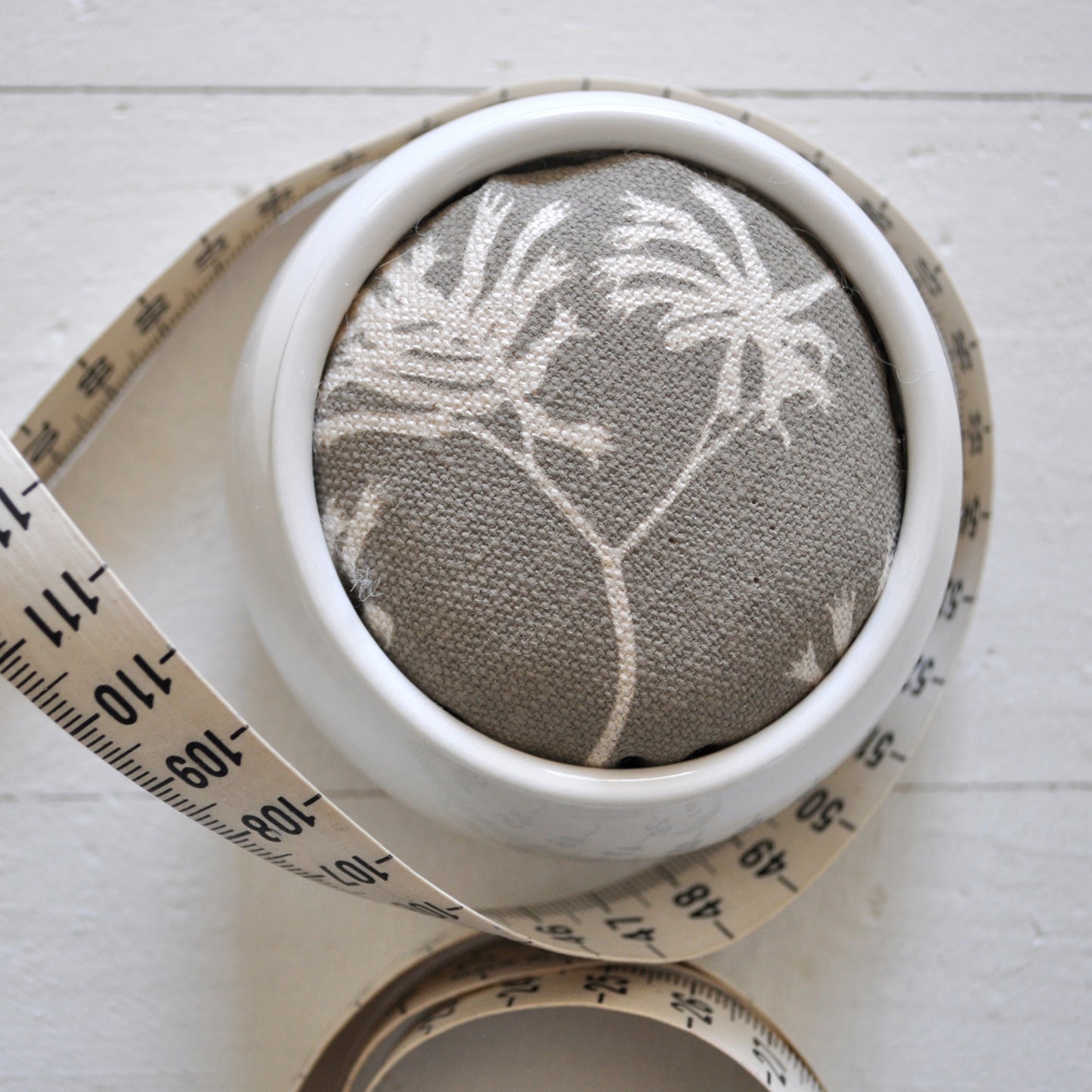 Pinch River ceramic pin cushion featuring Kangaroo Paw print in Aged Wood (colourway 2_v2). Close-up top view. Product image is styled with a measuring tape.