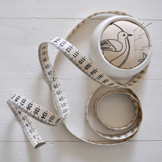 Pinch River ceramic pin cushion featuring Lyrebird print in Grey Bark (colourway 1). Top view. Product image is styled with a measuring tape and pins.