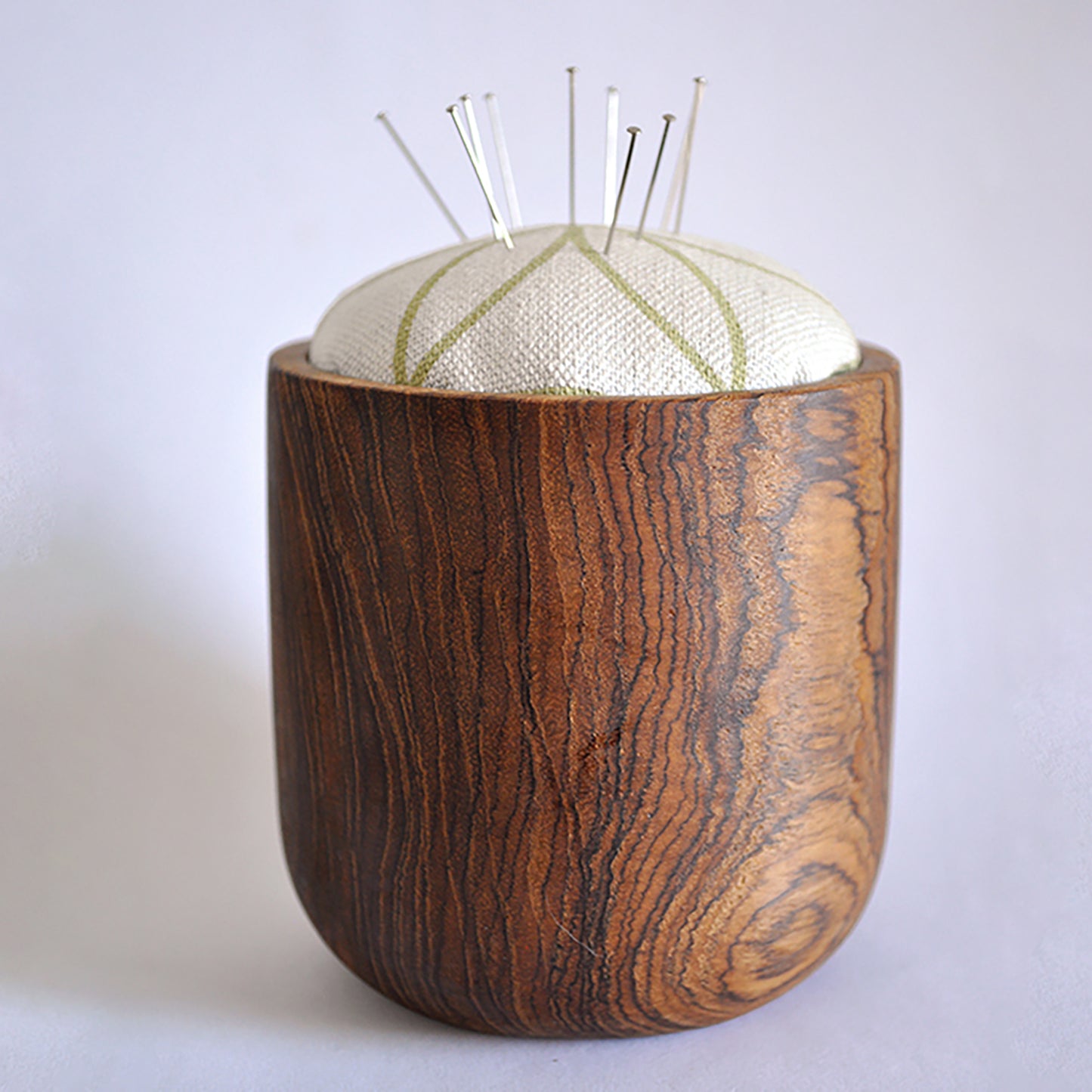 Pinch River teak pin cushion featuring Flower of Life print in Spring Green (colourway 1). Side view. Product image is styled with pins.