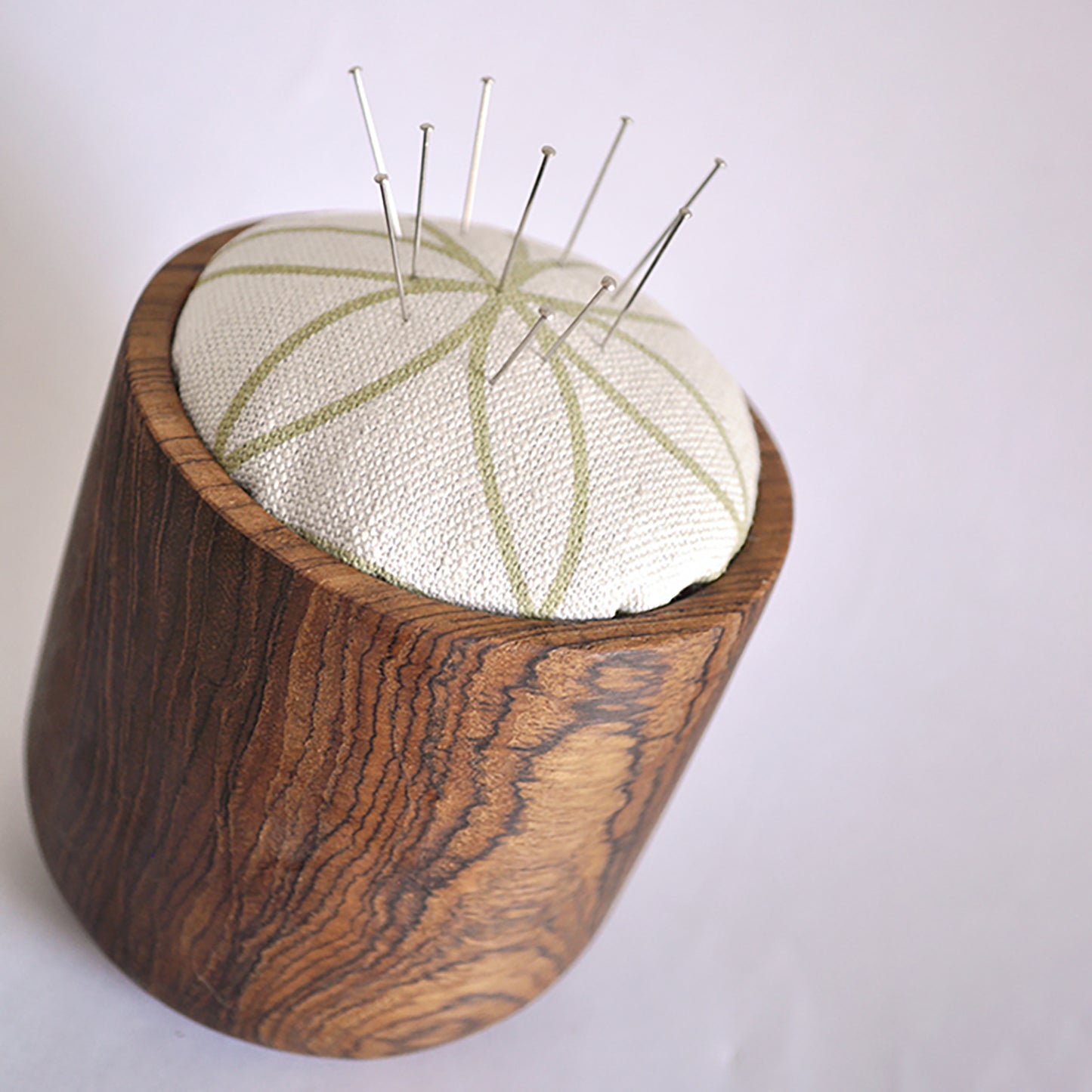 Pinch River teak pin cushion featuring Flower of Life print in Spring Green (colourway 1). Angled view. Product image is styled with pins.