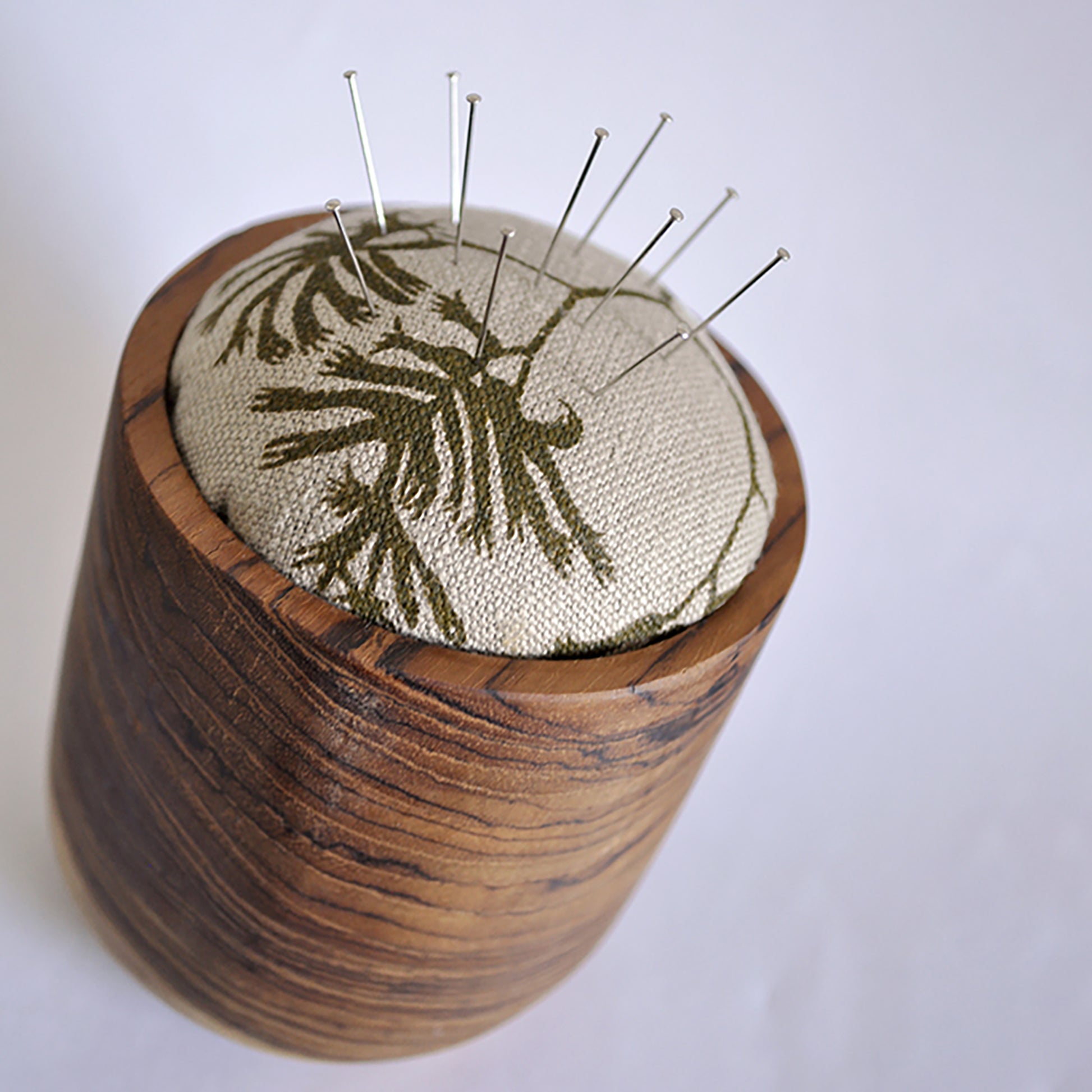 Pinch River teak pin cushion featuring Kangaroo Paw print in Desert Green (colourway 1). Angled view. Product image is styled with pins.