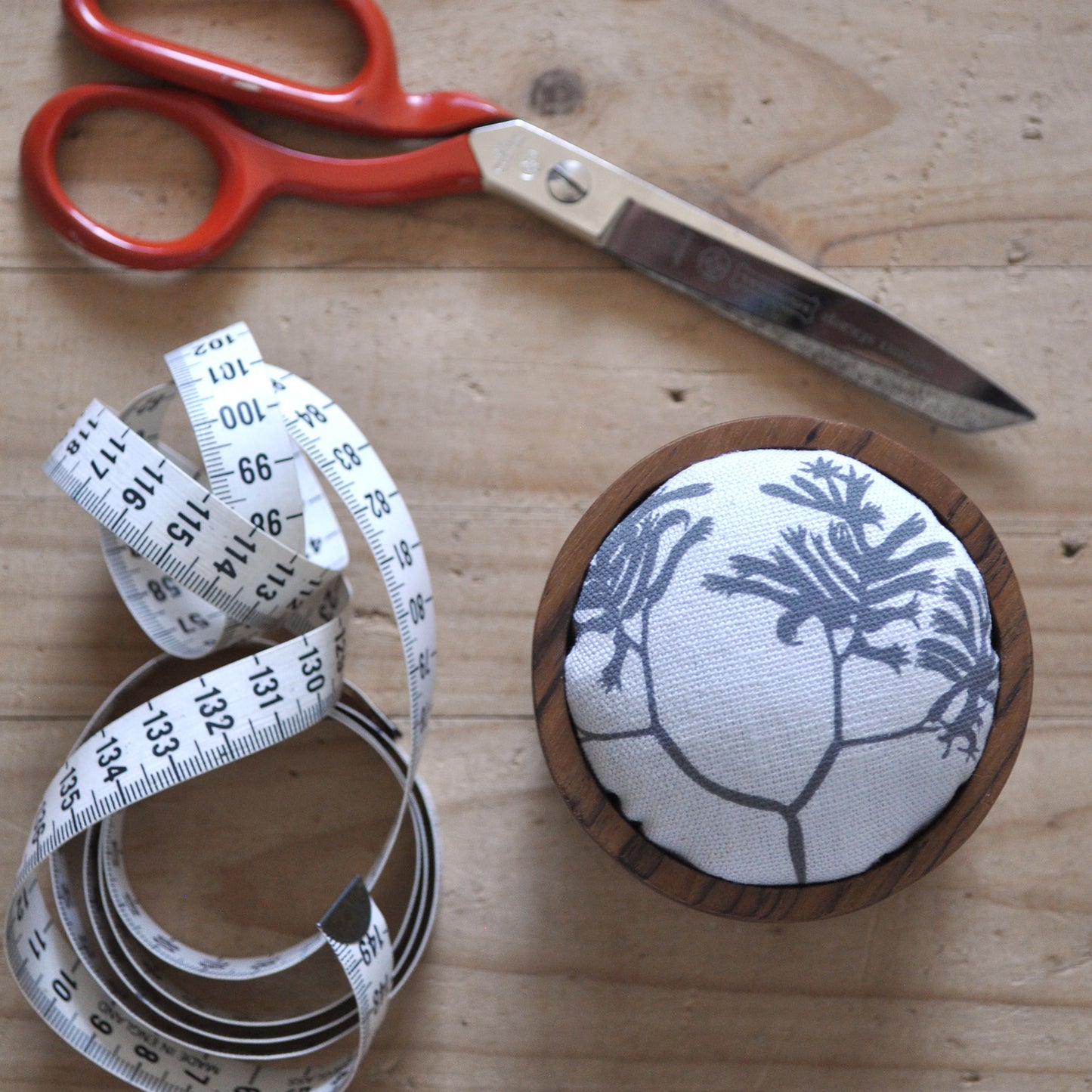 Pinch River teak pin cushion featuring Kangaroos Paw print in Tempest (colourway 3). Top view. Product image is styled with scissors and a measuring tape.