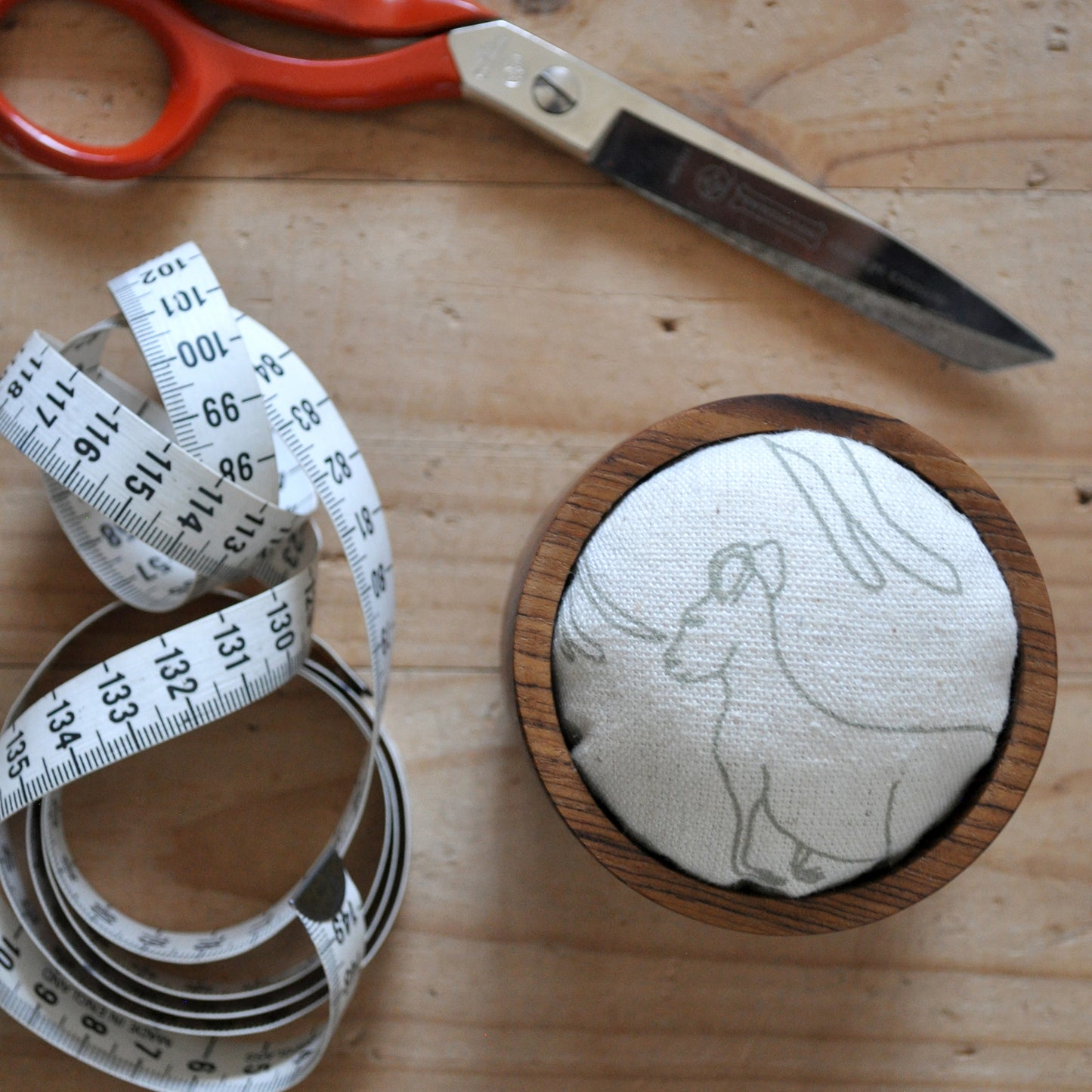 Pinch River teak pin cushion featuring Kangaroos print in Moss Green (colourway 1). Top view. Product image is styled with scissors and a measuring tape.