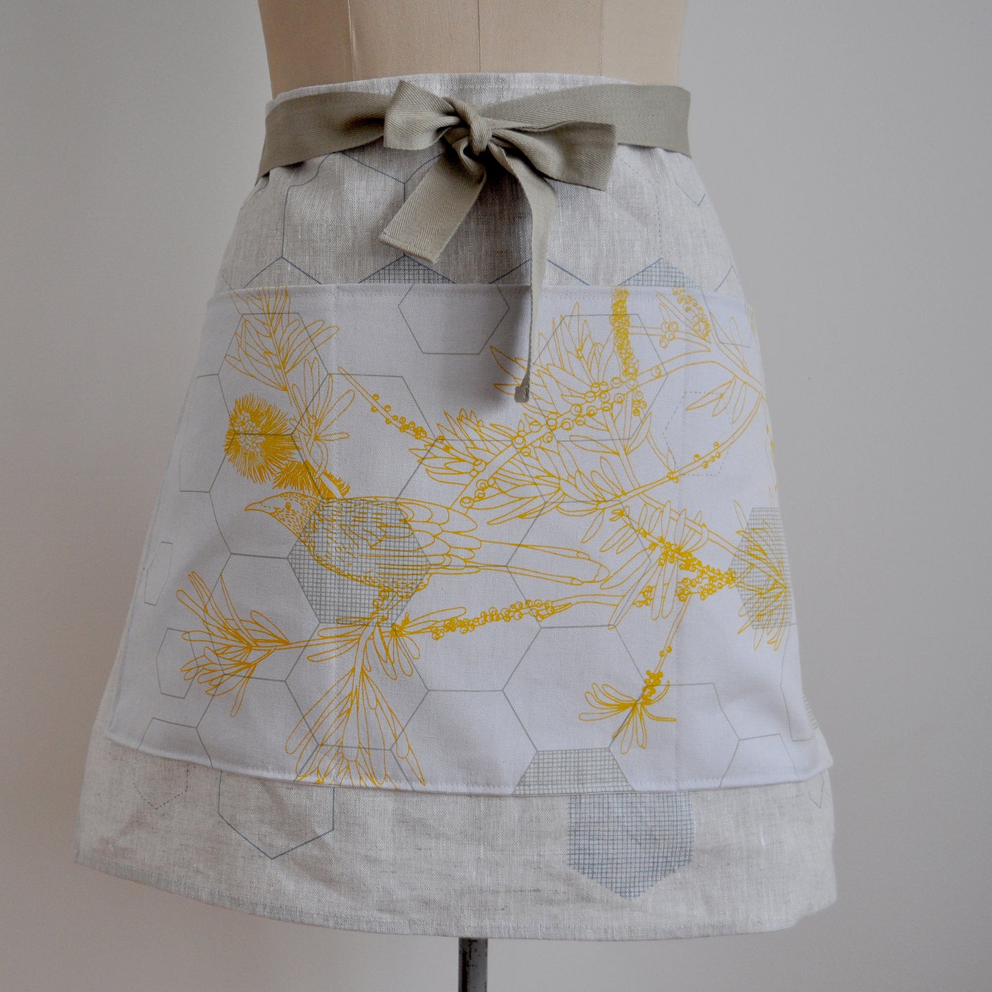 Pinch River waist apron / half apron No. 1 with pockets, on dressmakers dummy against a plain background. Front View. Close-up.